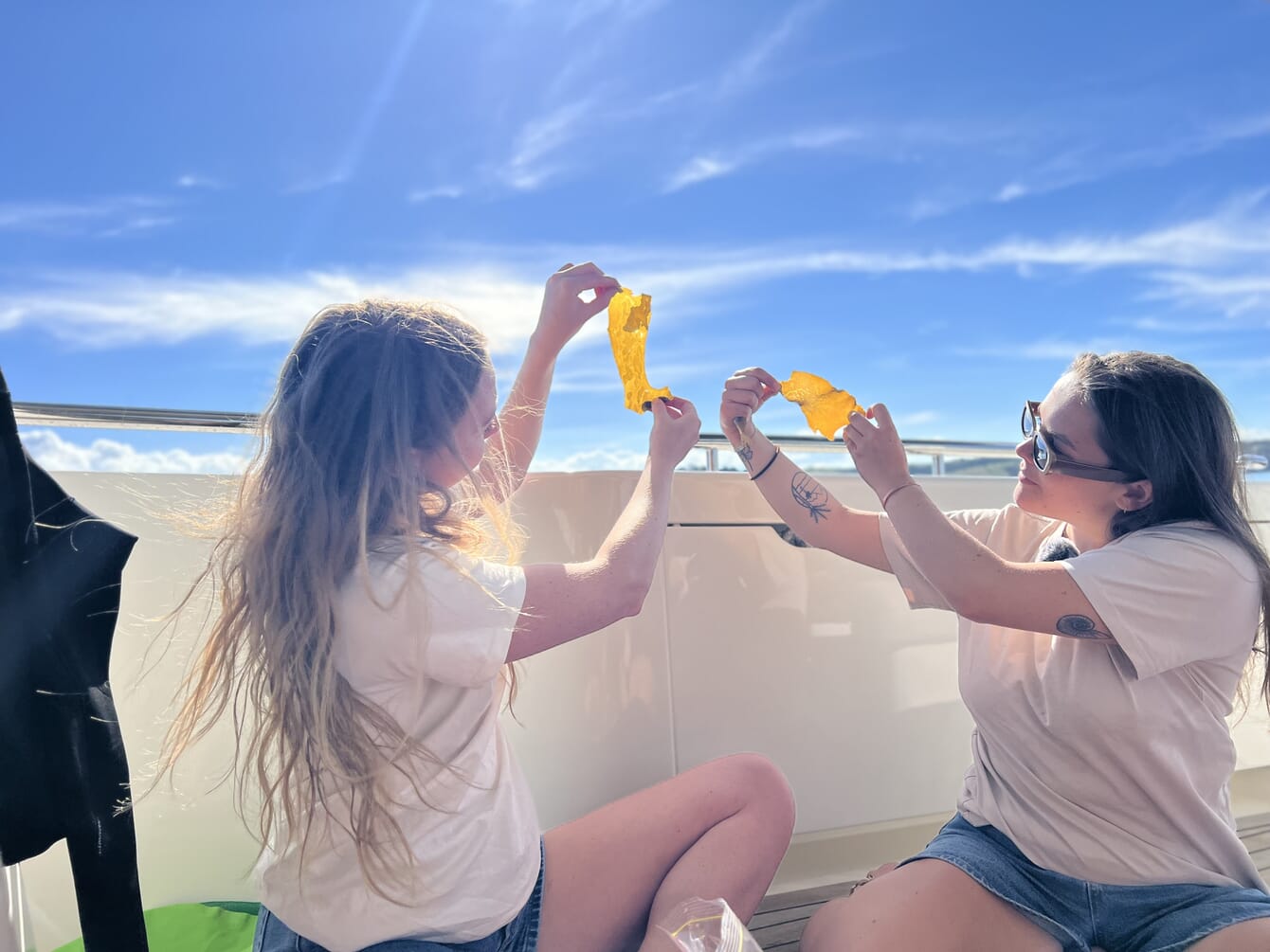Two women holding up a piece of kelp towards the sun on a boat.