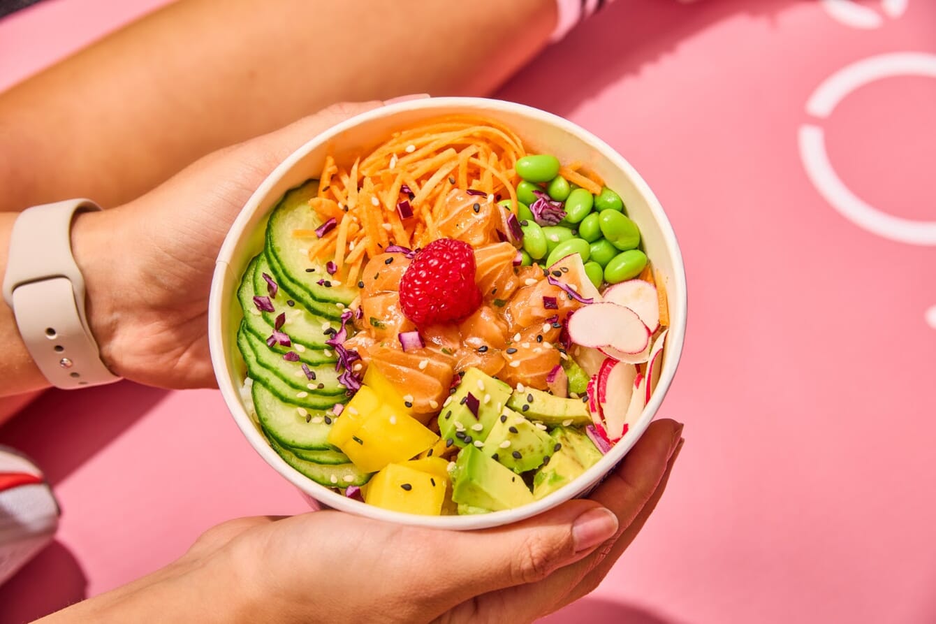 A person holding a poke bown with fresh salmon.