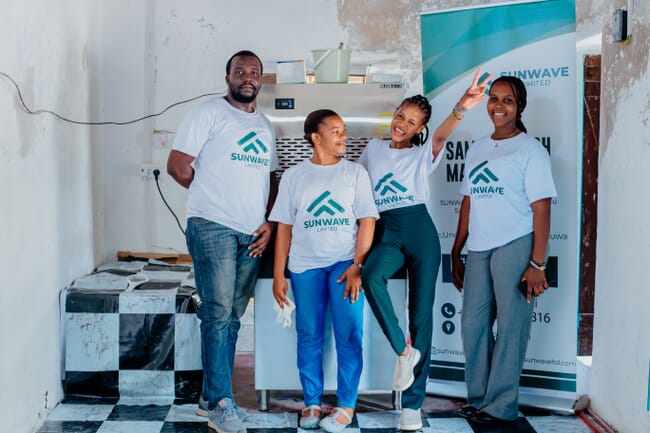 Four people standing beside a sign.