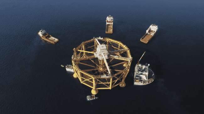 Aerial view of a large metal fish farming structure, surrounded by boats.