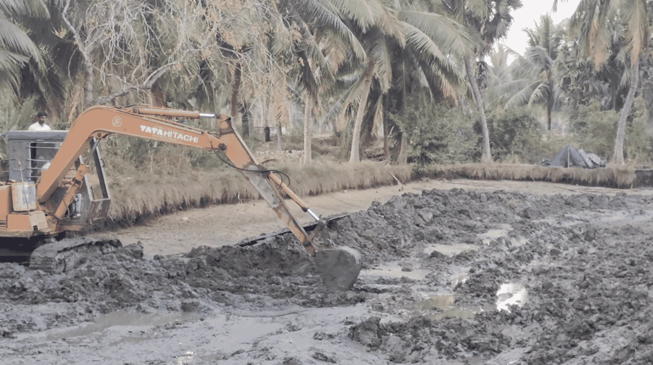 An excavator removing sludge from an empty shrimp pond.